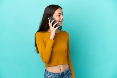 Mavi arka planda izole edilmiş genç bir Fransız kadın cep telefonuyla biriyle sohbet ediyor.
