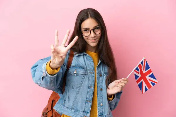 Young French girl holding an United Kingdom flag isolated on pink background happy and counting three with fingers