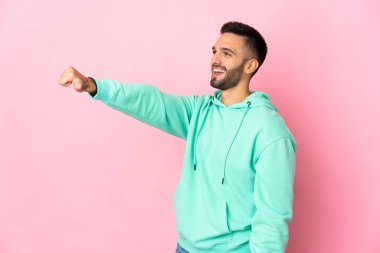 Pembe arka planda izole edilmiş genç beyaz bir adam baş parmak hareketi yapıyor.