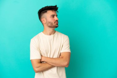 Mavi arka planda izole edilmiş genç beyaz adam yan tarafa bakıyor.