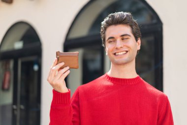 Dışarıda cüzdanını tutan genç yakışıklı adam mutlu bir ifadeyle.