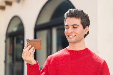 Dışarıda cüzdanını tutan genç yakışıklı adam mutlu bir ifadeyle.