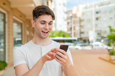 Genç yakışıklı adam cep telefonuyla mesaj ya da e-posta yolluyor.