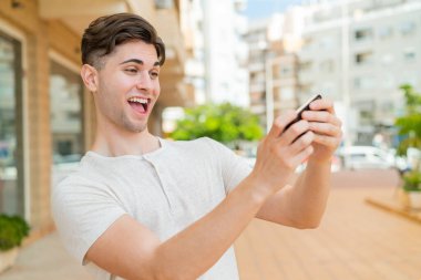 Genç yakışıklı adam cep telefonuyla oynuyor.