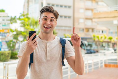 Dışarıda cep telefonu kullanan yakışıklı genç adam harika bir fikri işaret ediyor.