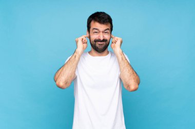 Mavi arka planda sakallı genç adam hayal kırıklığına uğramış ve kulaklarını kapatmış.