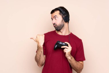 İzole edilmiş duvarın üzerinde oyun kumandasıyla oynayan adam mutsuz ve kenarı işaret ediyor.