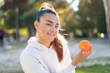 Genç, güzel esmer kadın elinde bir portakal tutuyor.