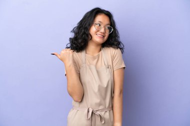 Mor arka planda izole edilmiş Asyalı restoran garsonu bir ürünü sunmak için yan tarafı işaret ediyor.