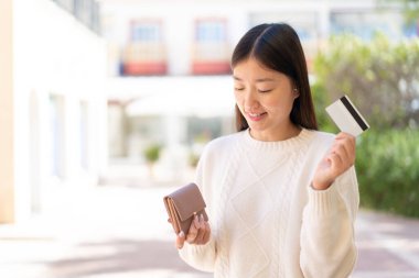 Dışarıdaki güzel Çinli kadın elinde cüzdan ve mutlu bir ifadeyle kredi kartı tutuyor.