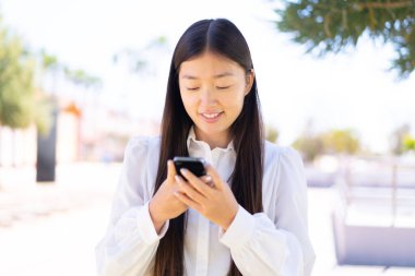 Dışarıdaki güzel Çinli kadın cep telefonuyla mesaj yolluyor.