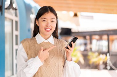 Dışarıdaki genç Çinli kadın cep telefonu kullanıyor ve onu işaret ediyor.