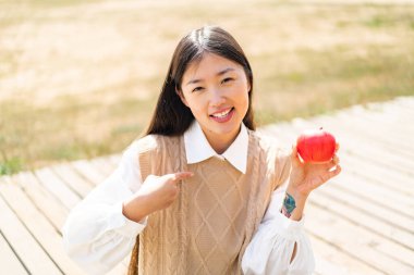 Açık havada elmalı genç bir Çinli kadın, yüzünde sürpriz bir ifade var.