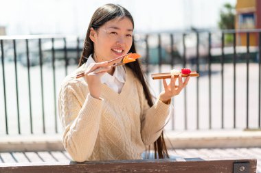 Genç Çinli bir kadın açık havada sashimi tutuyor.