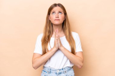 Bej arka planda izole edilmiş genç beyaz kadın avuç içlerini bir arada tutuyor. İnsan bir şey ister.
