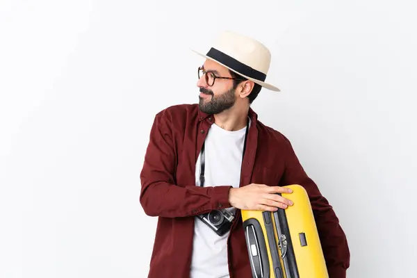 Traveler man man with beard holding a suitcase over isolated white background looking to the side