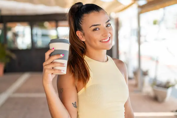Young pretty woman holding a take away coffee at outdoors smiling a lot