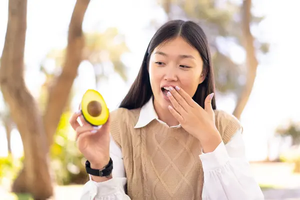 Pretty Chinese Woman Holding Avocado Outdoors Surprise Shocked Facial Expression — Stock Photo, Image