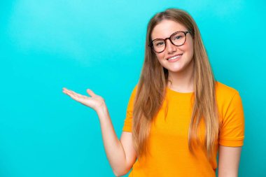 Mavi arka planda izole edilmiş genç beyaz kadın bir ilan vermek için avucunun içinde hayali bir fotokopi makinesi tutuyor.