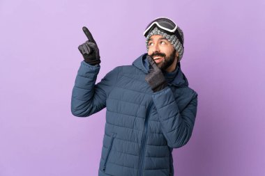 İzole edilmiş mor arka planda snowboard gözlüklü kayakçı, işaret parmağıyla işaret etmek harika bir fikir.