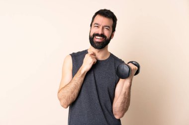 Beyaz sakallı sporcu arka planda halter kaldırarak gülüyor.