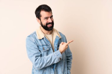 İzole edilmiş arka planda sakallı beyaz bir adam bir ürünü sunmak için kenarı işaret ediyor.