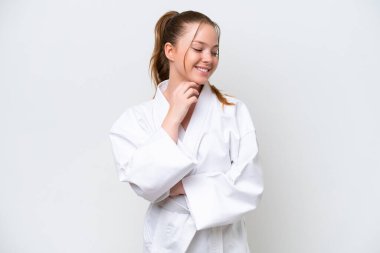 Beyaz arka planda karate yapan genç beyaz bir kız yan bakıp gülümsüyor.