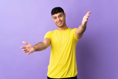 Mor arka planda izole edilmiş genç Kolombiyalı adam sunar ve davet eder.