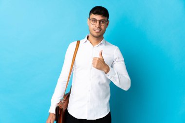 Kolombiyalı genç bir adam mavi arka planda izole edilmiş bir şekilde el hareketi yapıyor.