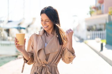Genç bir kadın açık havada kahvesini yudumlarken zaferi kutluyor.