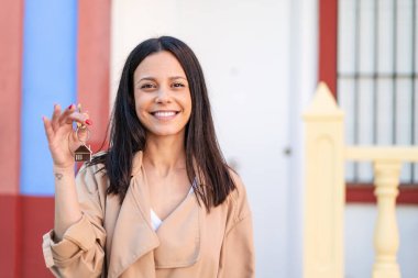 Açık havada elinde mutlu bir ifadeyle evin anahtarlarını tutan genç bir kadın.