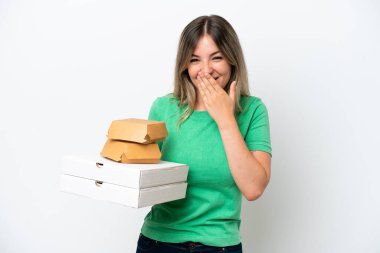 Beyaz arka planda hazır yemek tutan genç Romen kadın mutlu ve ağzı kapalı gülümsüyor.