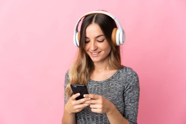 Genç Romen kadın pembe arka planda izole edilmiş müzik dinliyor ve cep telefonu arıyor