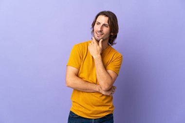 Mor arka planda soyutlanmış genç yakışıklı adam yana bakıyor ve gülümsüyor.