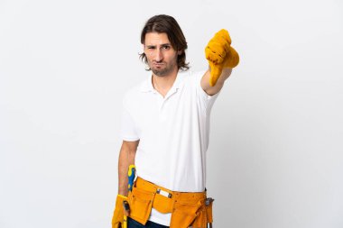 İzole edilmiş arka planda genç elektrikçi başparmağını negatif ifadeyle aşağı gösteriyor.