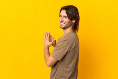 Genç yakışıklı adam sarı arka planda bir şeyler çeviriyor.