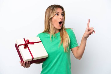 Genç Uruguaylı kadın elinde beyaz arka planda izole edilmiş bir hediye tutuyor. Çözümün farkına varmak için parmağını kaldırıyor.