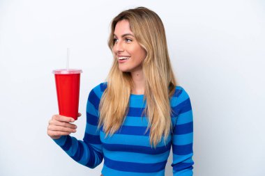 Young Uruguayan woman drinking soda isolated on white background looking to the side and smiling