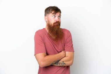 Uzun sakallı kızıl saçlı adam, beyaz arka planda izole edilmiş. Omuzlarını kaldırırken şüpheli hareketler yapıyor.