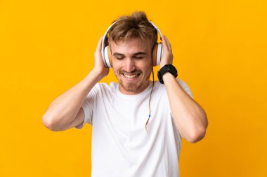 Sarı arka planda izole edilmiş yakışıklı sarışın adam müzik dinliyor.