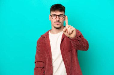 Beyaz tenli yakışıklı adam mavi arka planda izole edilmiş ciddi bir ifadeye sahip birini sayıyor.