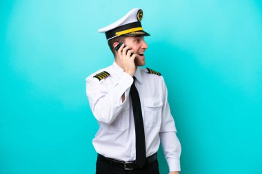 Kafkasyalı uçak pilotu mavi arka planda izole edilmiş cep telefonuyla sohbet ediyor.