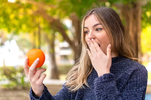 年轻漂亮的罗马尼亚女人在户外拿着橙子 脸上带着惊讶和震惊的表情 — 图库照片