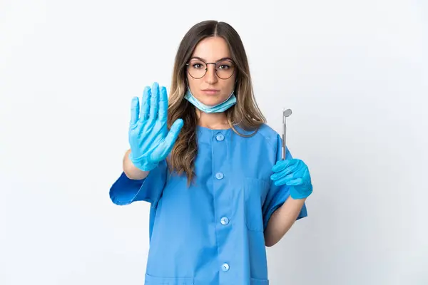 罗马尼亚女牙医举着工具 在粉色背景下被隔离 摆出停止姿势 — 图库照片