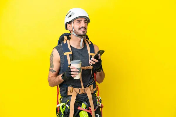 Jonge Kaukasische Bergbeklimmer Man Geïsoleerd Gele Achtergrond Houden Koffie Mee — Stockfoto