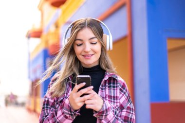 Genç ve güzel Romen kadın açık havada müzik dinliyor ve cep telefonu arıyor