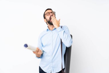 İzole edilmiş beyaz arka planda sakallı genç mimar esniyor ve ağzını eliyle açık tutuyor.