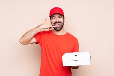 Elinde pizza tutan genç bir adam telefon jesti yapıyor. Bana geri dönüş işareti ver.