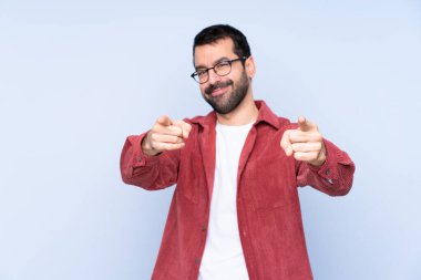 Mavi arka plan üzerinde kadife ceket giyen genç beyaz adam gülümserken seni işaret ediyor.