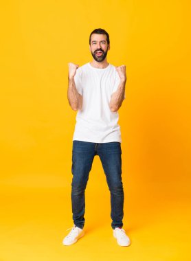 Sakallı, izole edilmiş sarı arka planda zaferi kutlayan bir adamın uzun pozu.